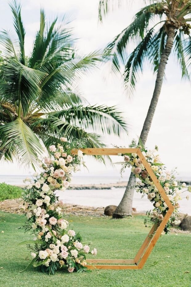 Beach wedding arch with wood, green foliage, and blooming flowers