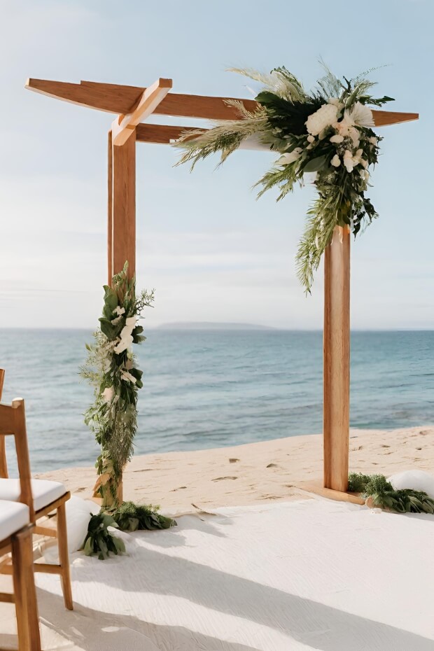 Beach wedding arch with wooden poles and green foliage