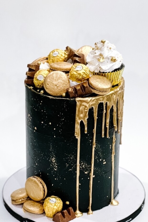 Black and gold wedding cake with chocolate and gold flakes, topped with golden drizzle