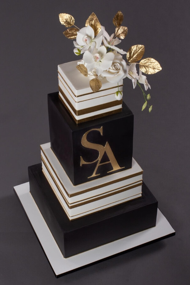 Elegant black and gold wedding cake with floral arrangement and gold frosting