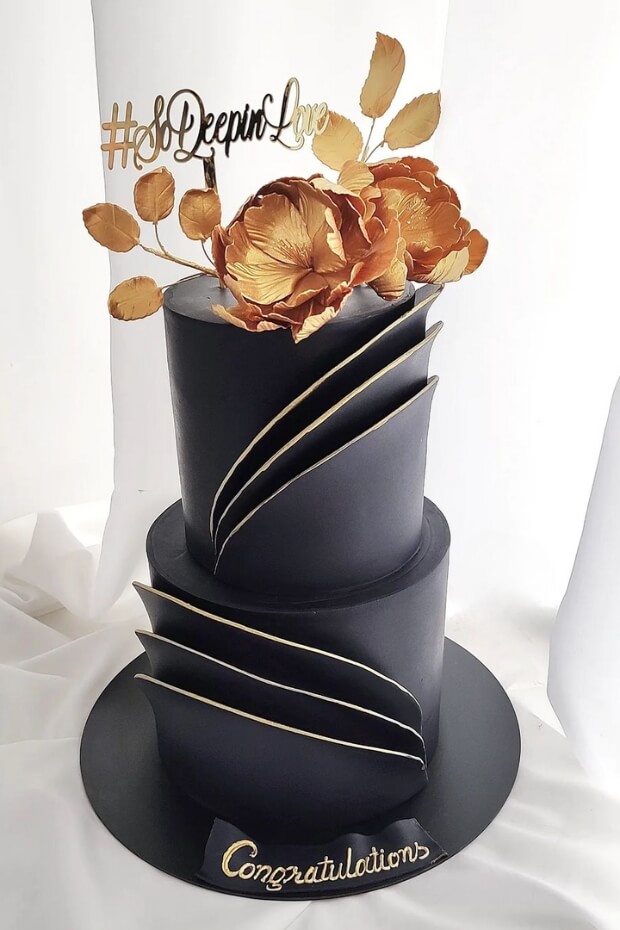 Chic black and gold wedding cake with gold flower on white surface