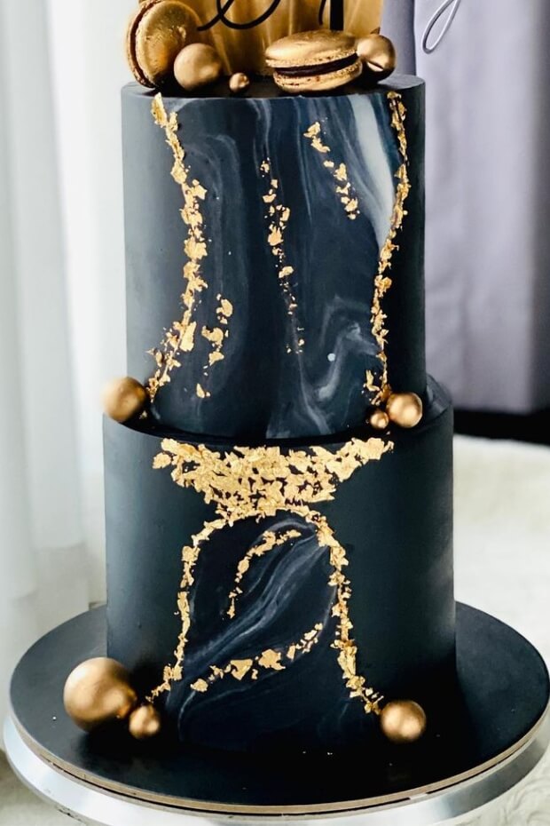 Elegant black and gold wedding cake with gold macarons and intricate gold leaf details