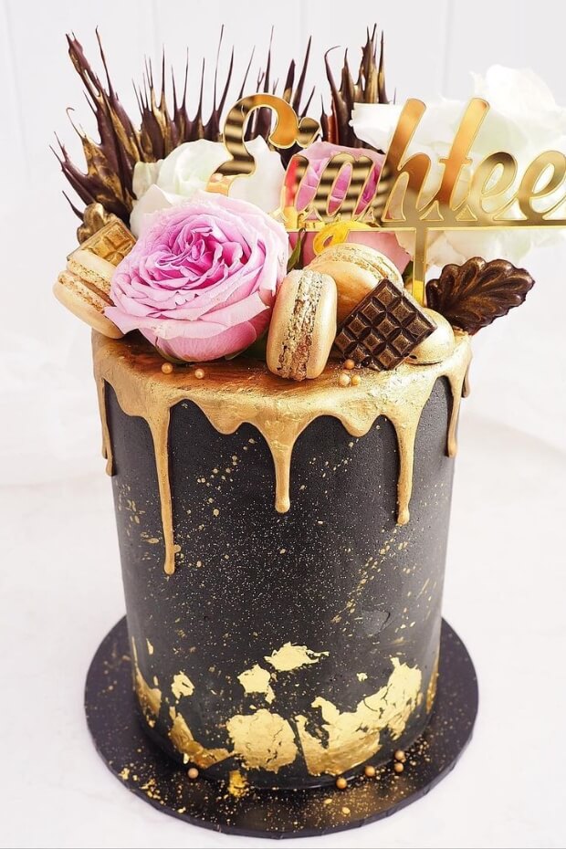 Elegant black and gold wedding cake with golden glaze and floral arrangement on top