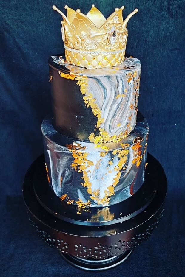 Regal black and gold wedding cake with intricate gold leaf details and crown decoration