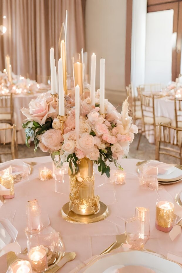 Blush pink and gold wedding centerpiece with vase of flowers and candles