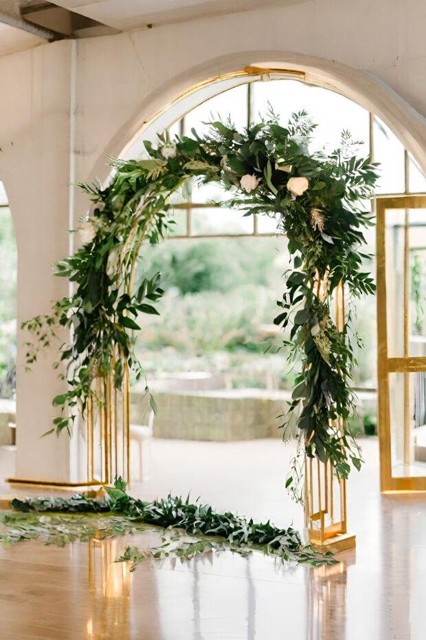 Gold wedding arch with lush greenery and white flowers