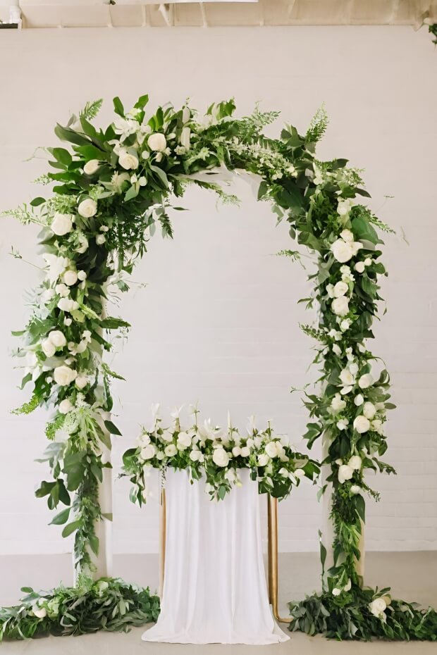 Wedding arch adorned with green foliage and white flowers in a golden frame