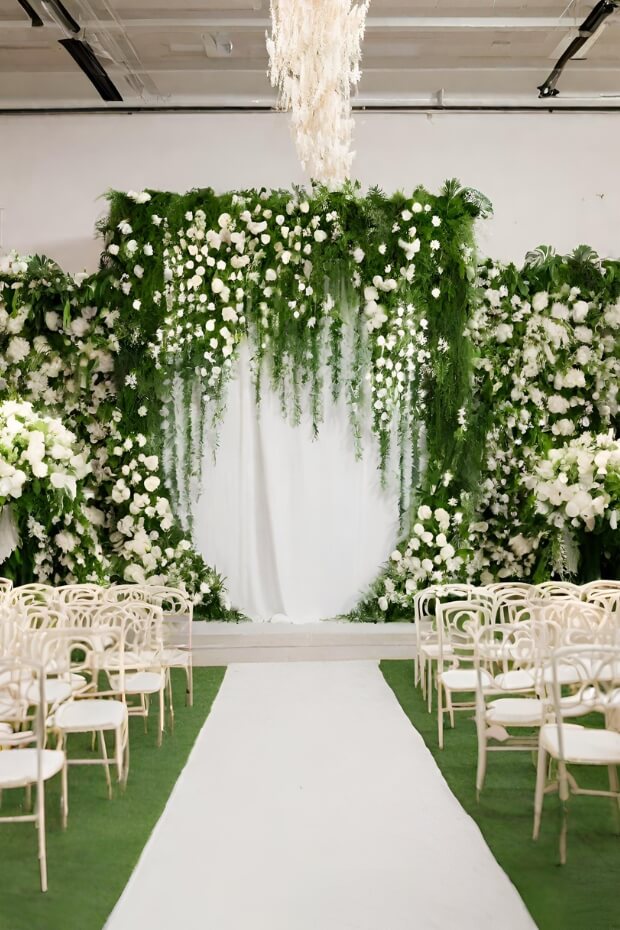 Greenery-covered archway with white chairs and aisle