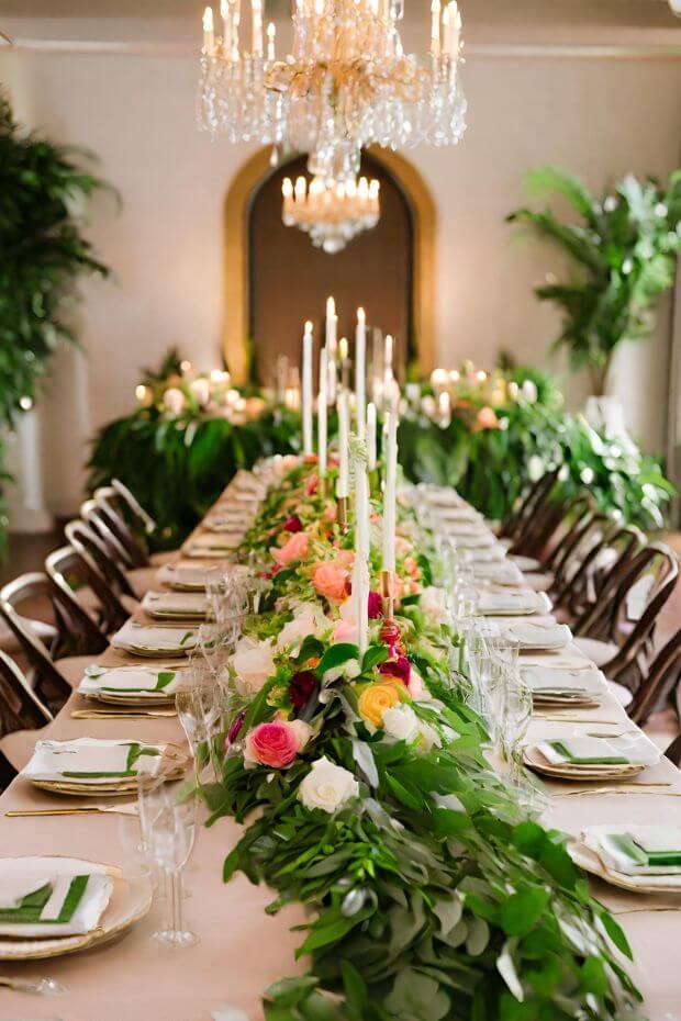 Long dining table set with white tablecloth, place settings, and elegant green and white candle centerpieces