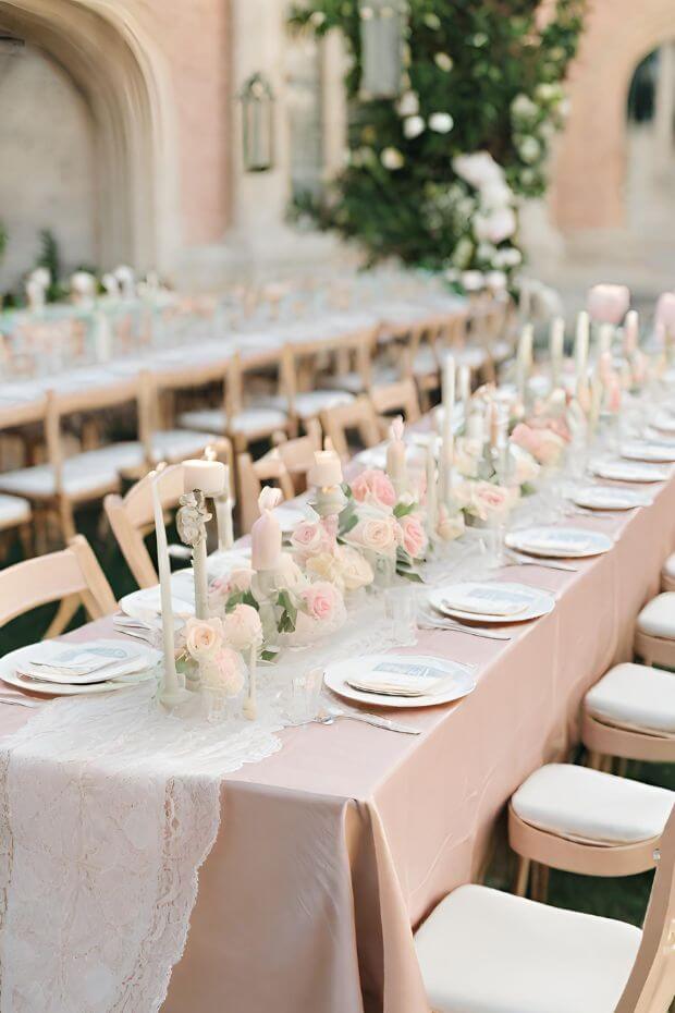 Pink table runner with white lace tablecloth and various centerpieces including candles and flowers