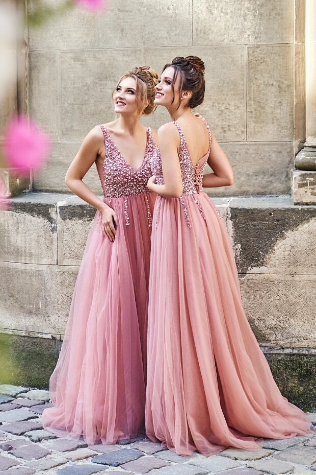 Two women in pink and gold dresses against pink wall