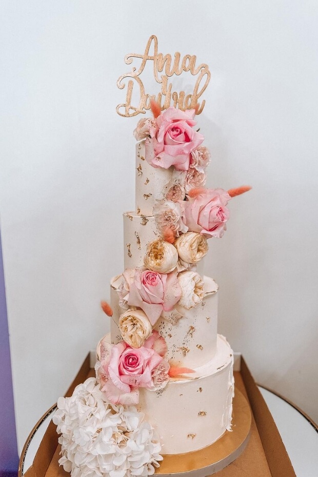 Wedding cake adorned with pink and white flowers on wooden table