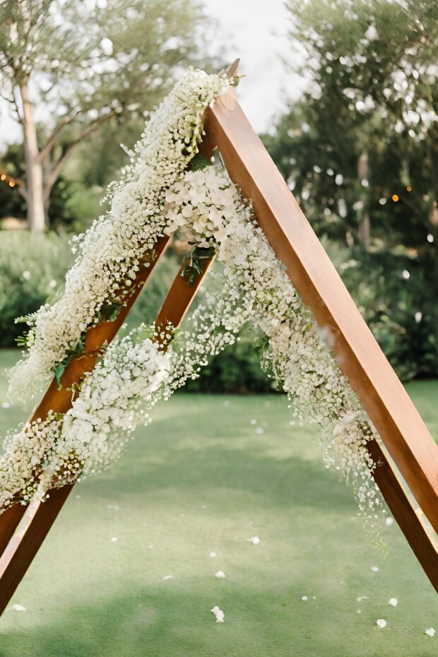 Triangular wooden wedding arch with lush greenery and baby's breath