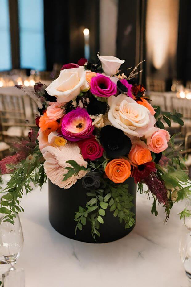 Black vase centerpiece with pink, white, and red blooms on dining table