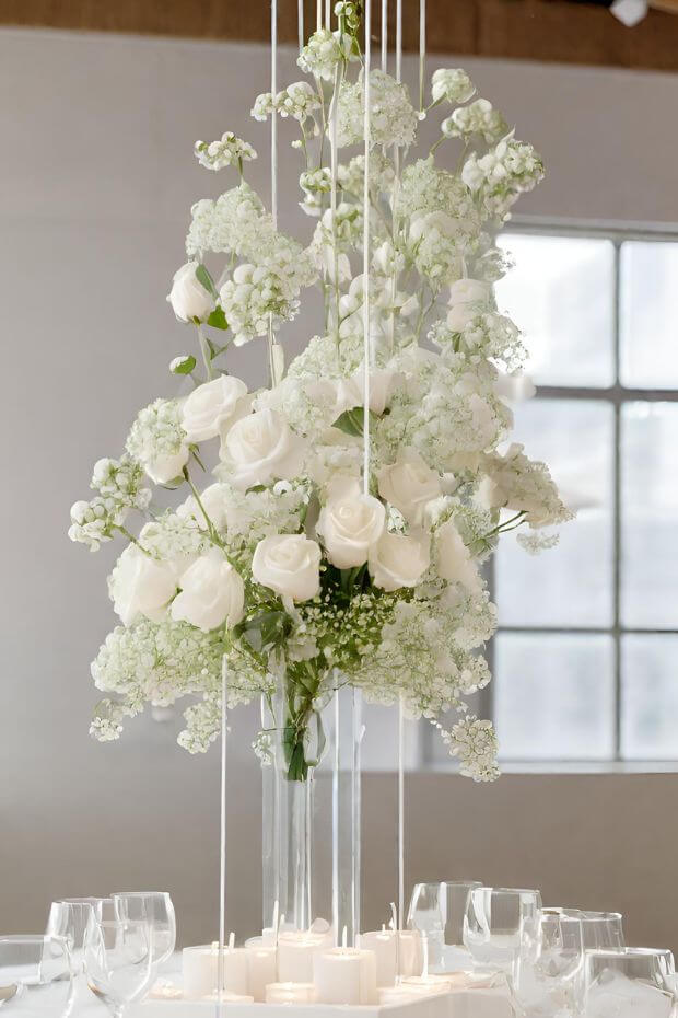 Clear vase centerpiece with white roses and greenery on white dining table