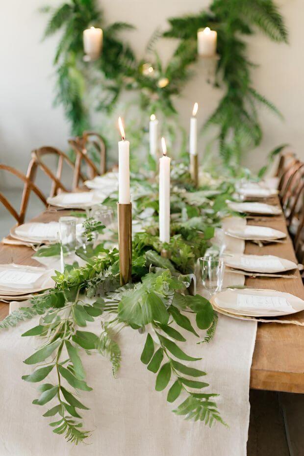 White linen tablecloth with gold candlesticks and green leaf arrangements