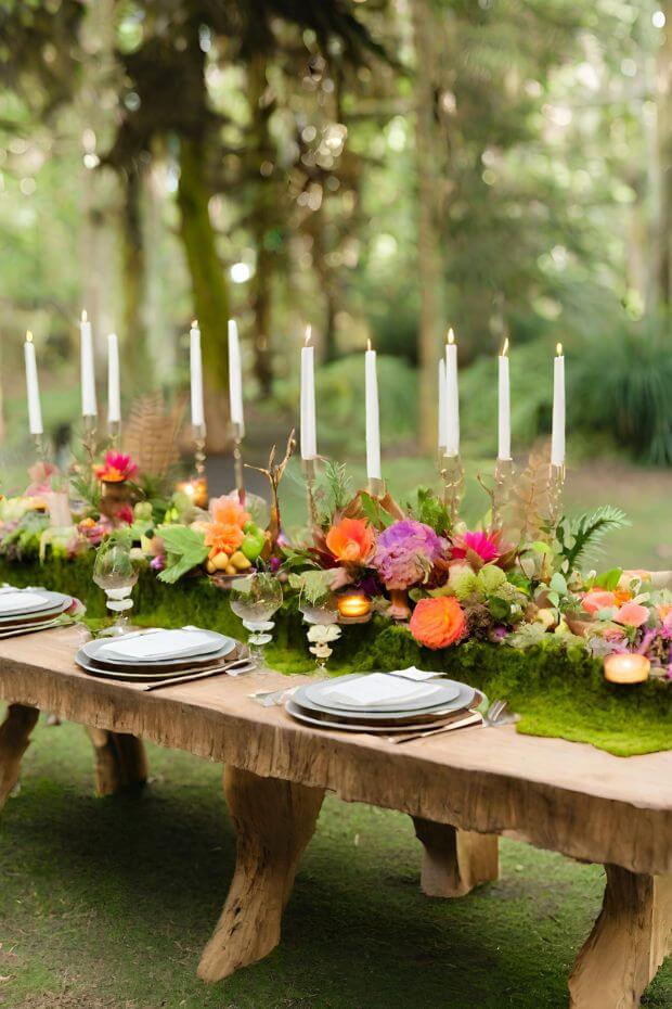 Wooden table surrounded by moss with colorful flowers arranged on top