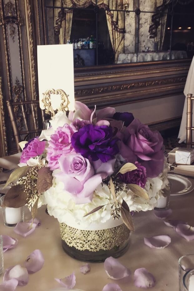 Luxurious wedding setup with purple and gold centerpiece and elegant chair decorations