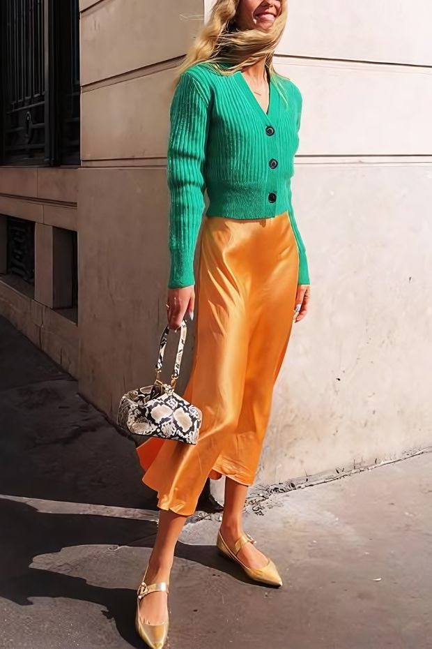 Bold fall wedding guest outfit with green cropped cardigan, yellow midi skirt, flats, and snakeskin print bag