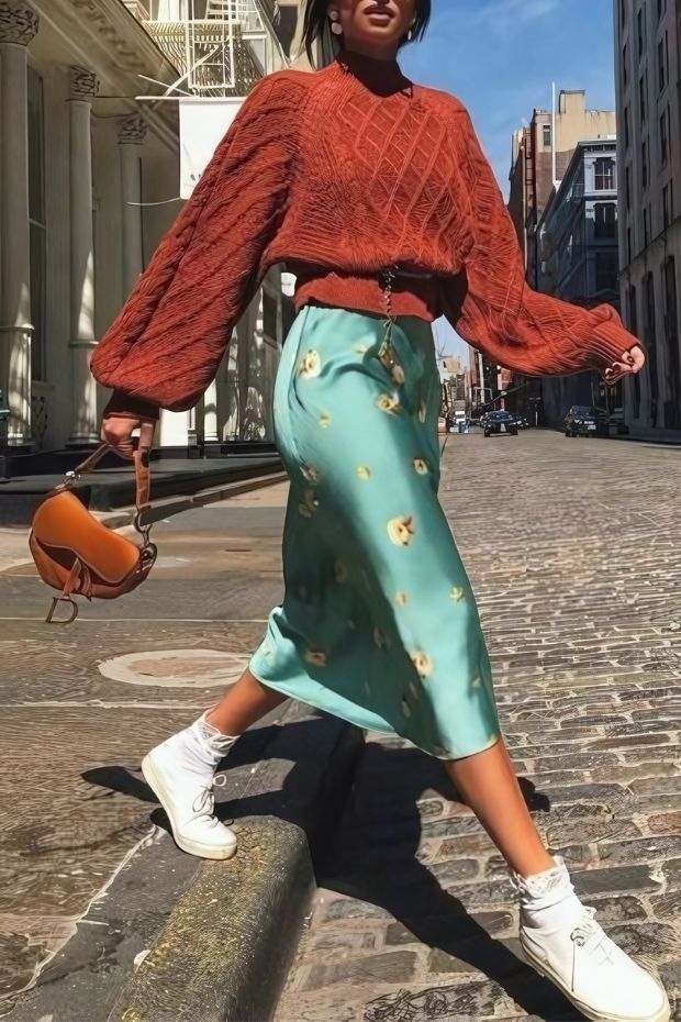Casual fall wedding guest outfit with rust cropped sweater, green printed skirt, sneakers, socks, and cognac mini bag
