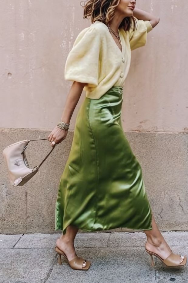 Dreamy fall wedding guest look with green satin midi skirt, ivory blouse, nude mules, and beige bag