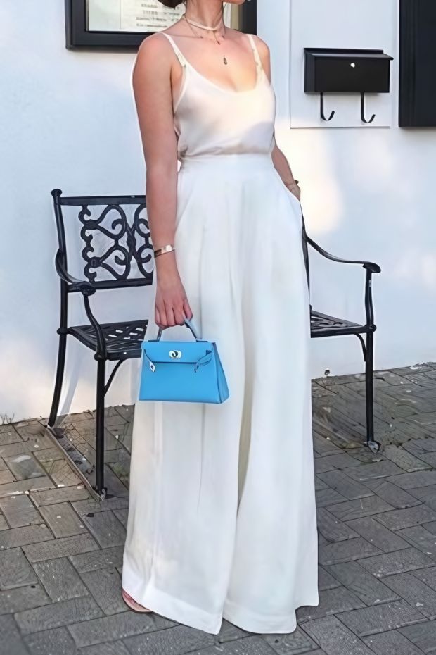 Casual summer wedding guest look with spaghetti strap top, white palazzo pants, and bold blue bag