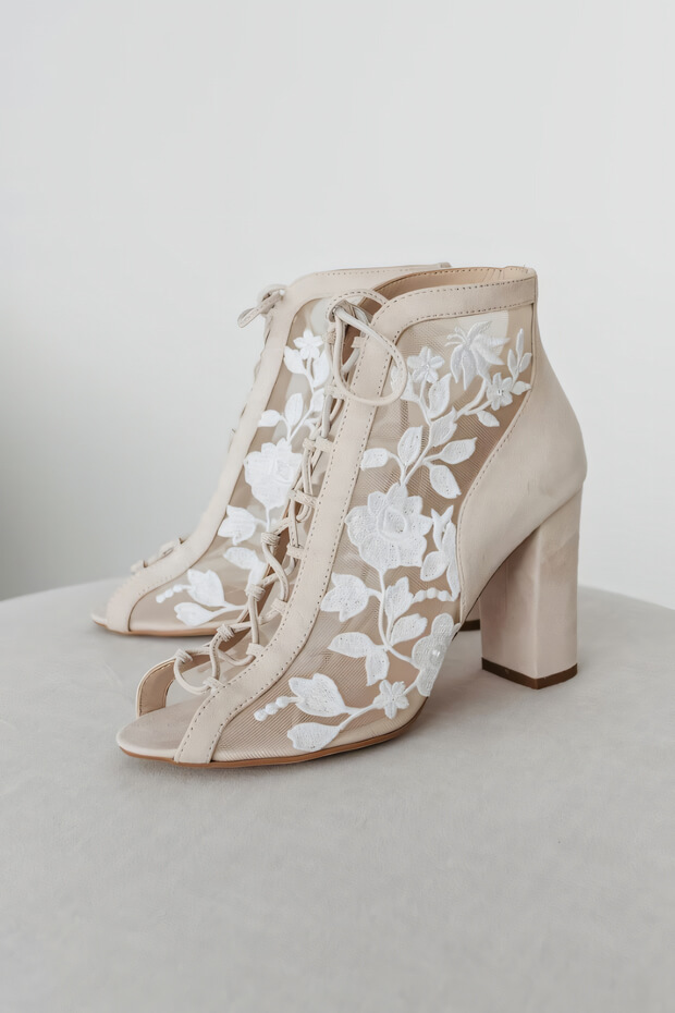 White bohemian-style ankle boots with lace-up closure and intricate floral embroidery.
