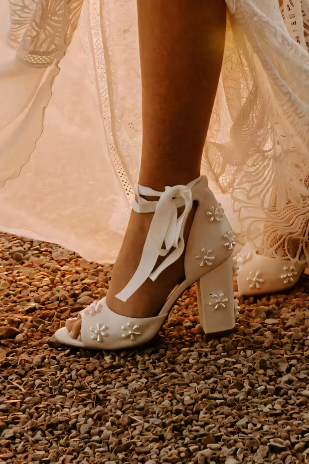 White shoes with floral design, ankle strap, leather, and block heel.