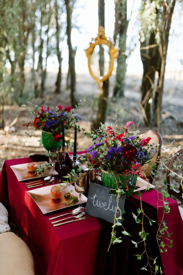 Moody enchanted forest wedding tablescape with crimson tablecloth, bright floral centerpiece